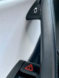 White Tesla door panel showing the electronic door-open button and a manual release lever marked with a red warning sticker.